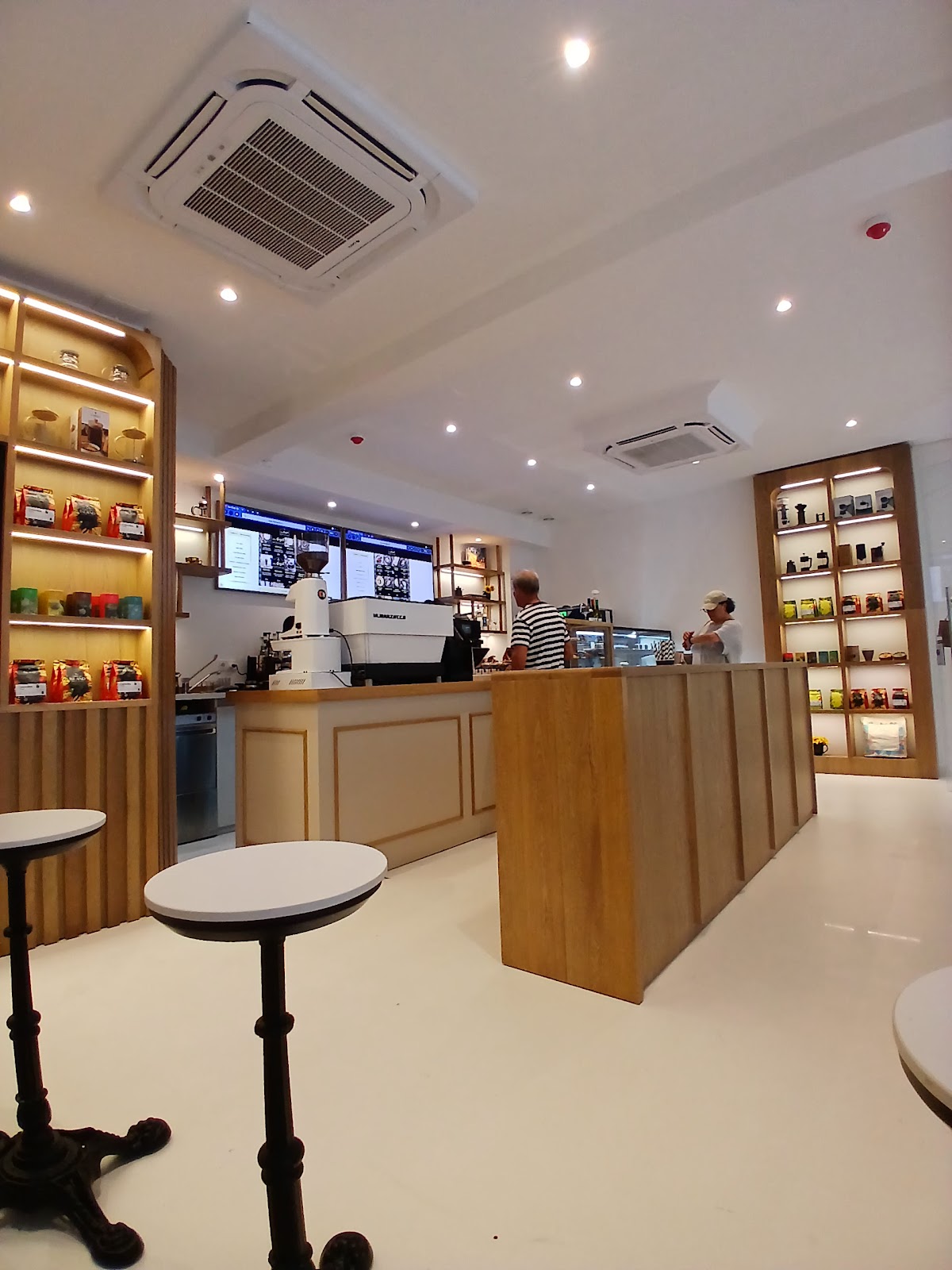 Inside the cafe — oak counter, espresso machine and lit arched shelves of coffee bags