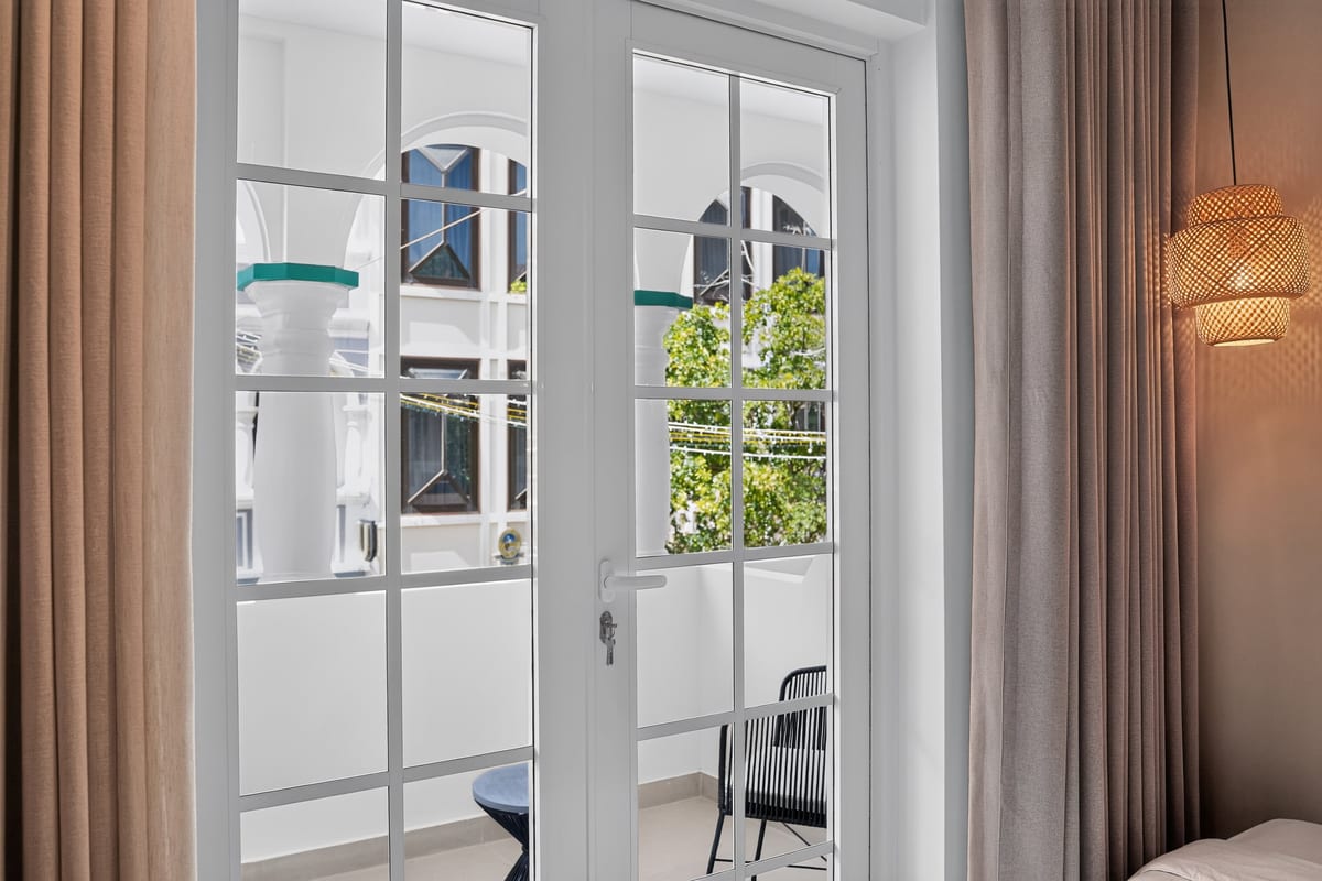 The glazed balcony doors close up, their white bars framing the arcade, a green tree and the painted house opposite