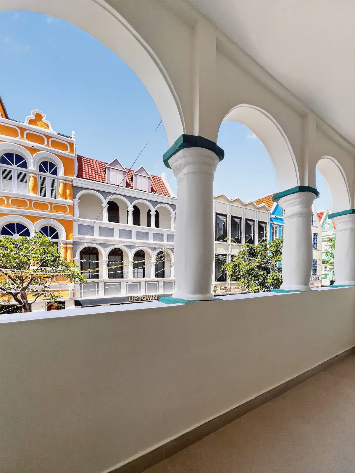 Looking along the private balcony through the white arches of the 1892 arcade at the yellow and white painted merchant houses of Breedestraat