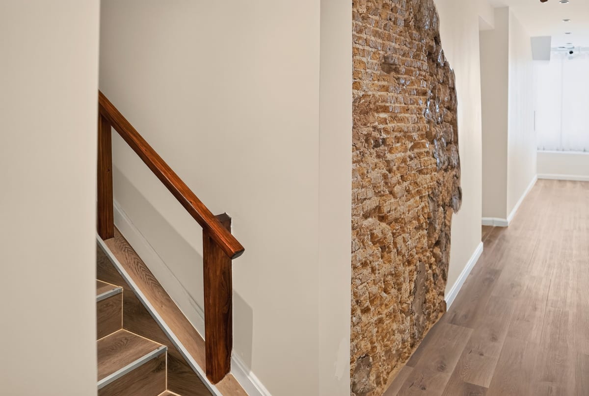 The staircase and a corridor where a panel of the original 1892 rubble stone wall has been left bare