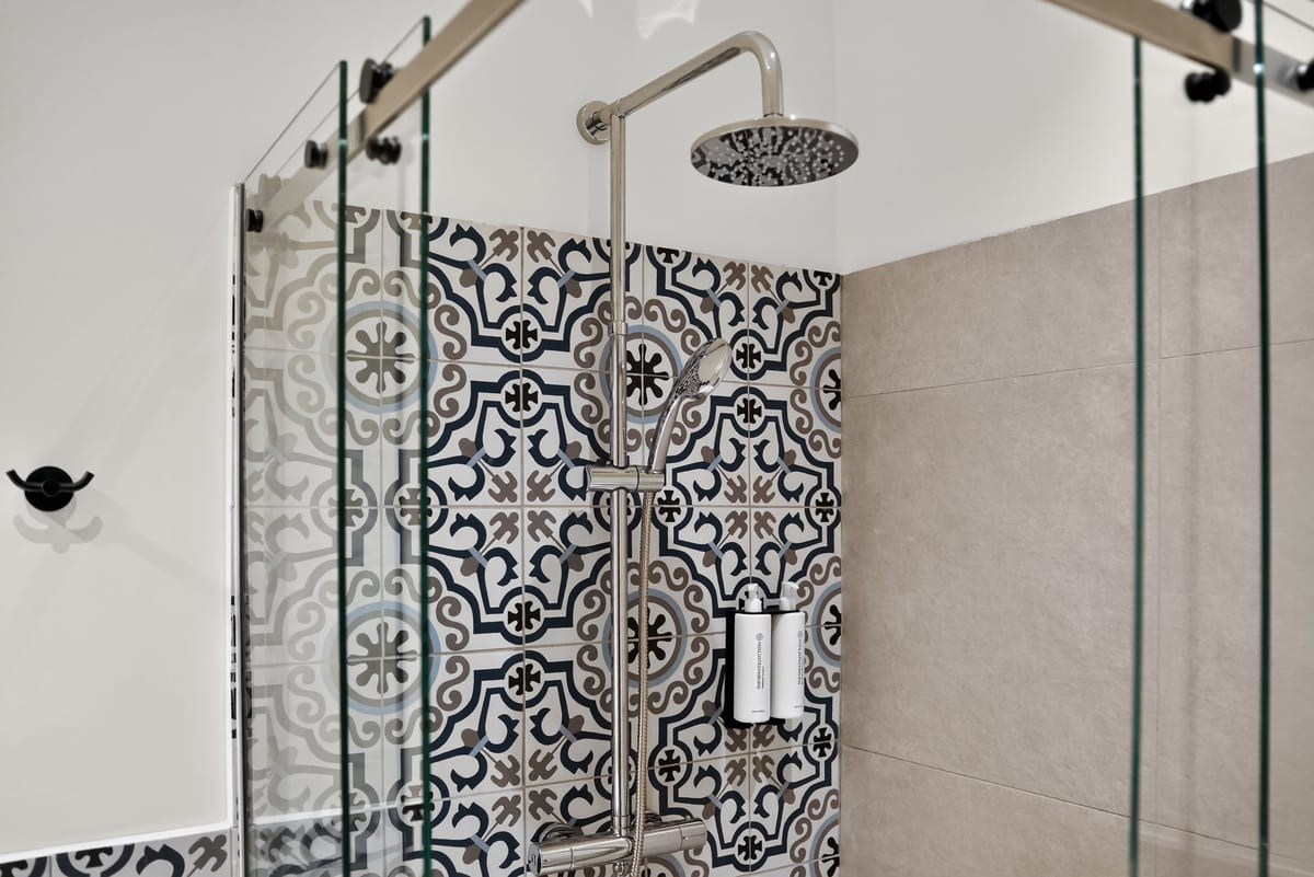 A brushed rain shower head and hand shower against a wall of cobalt and sand majolica, seen through the glass screen