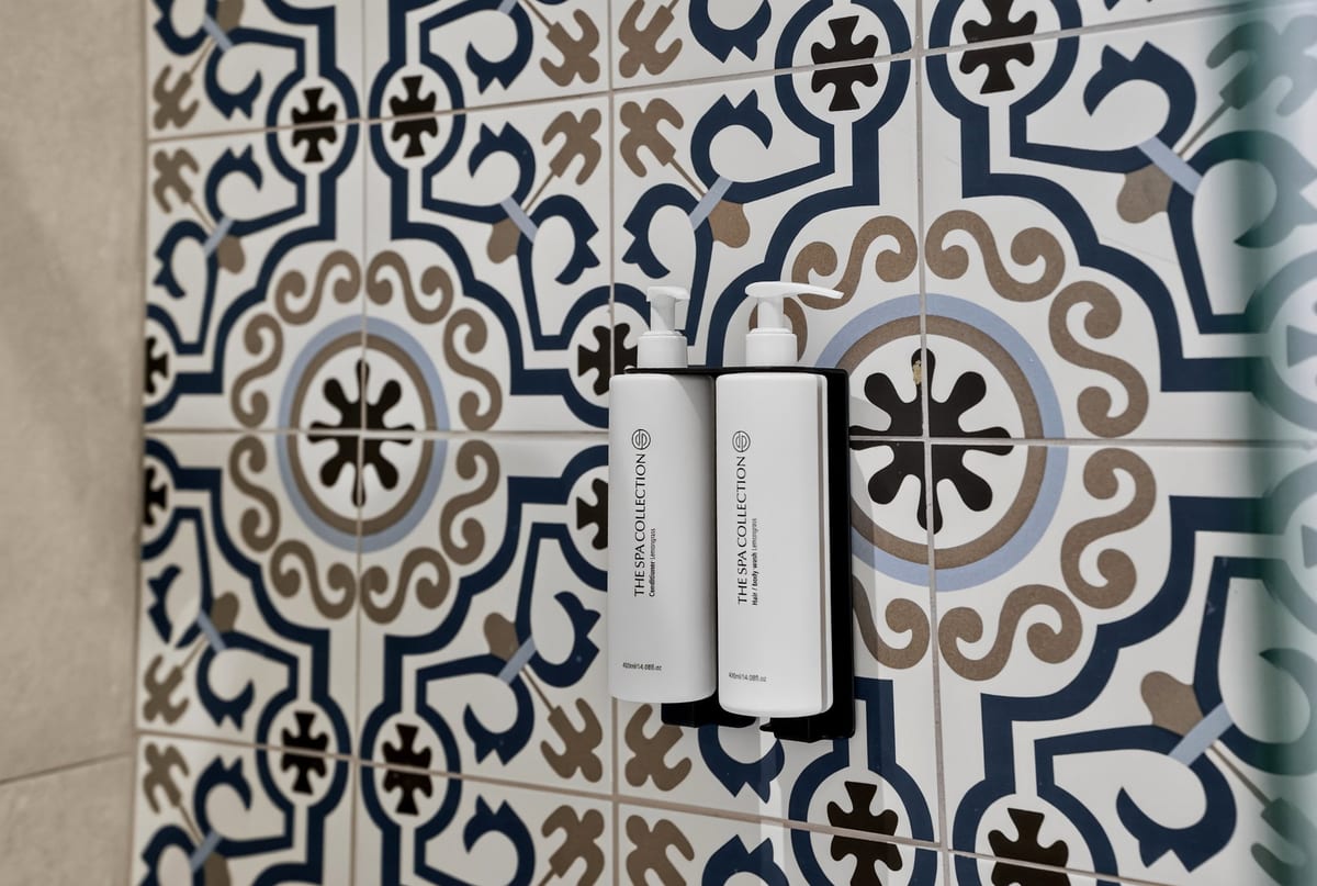 A wall of majolica in a Signature King Room shower, cobalt, sand and black pattern on cream, with two white amenity bottles on a black bracket
