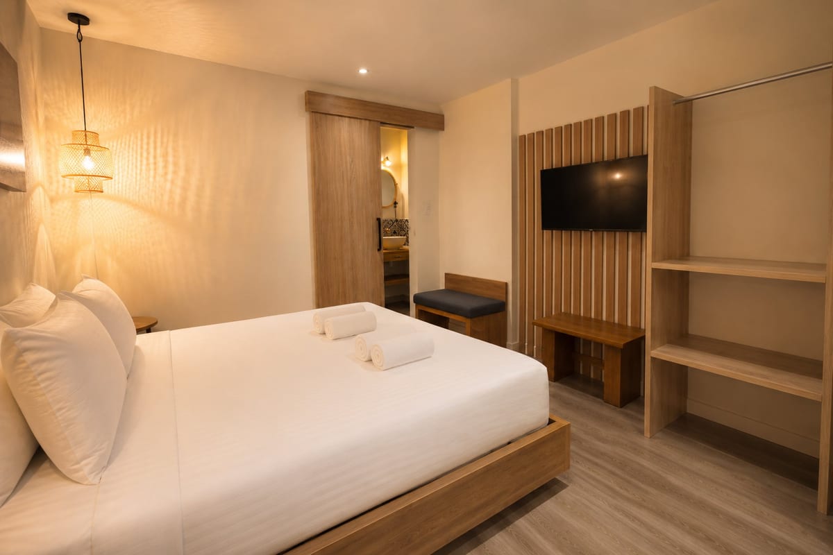 The room by lamplight: king bed, slatted television wall, open shelving and the bathroom through the doorway