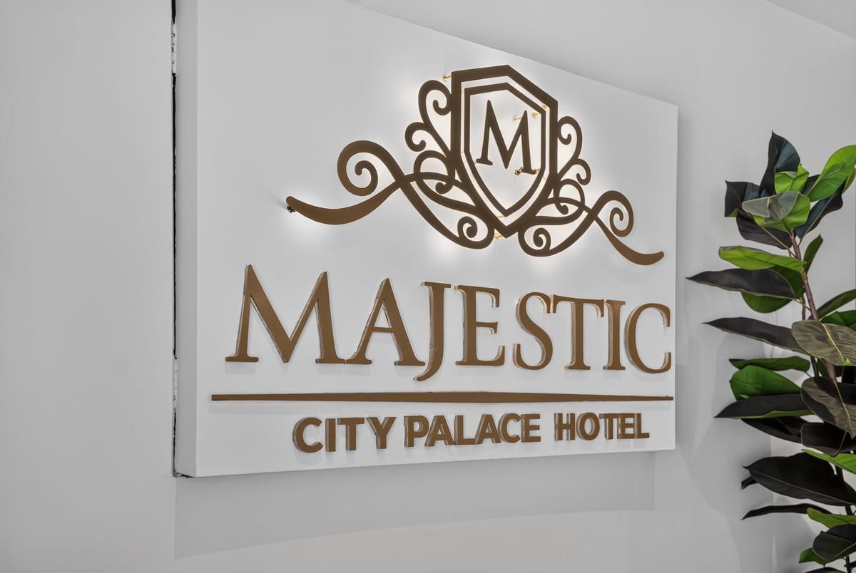 The Majestic City Palace crest in gold on the lobby wall, lit from above beside a dark leaved plant