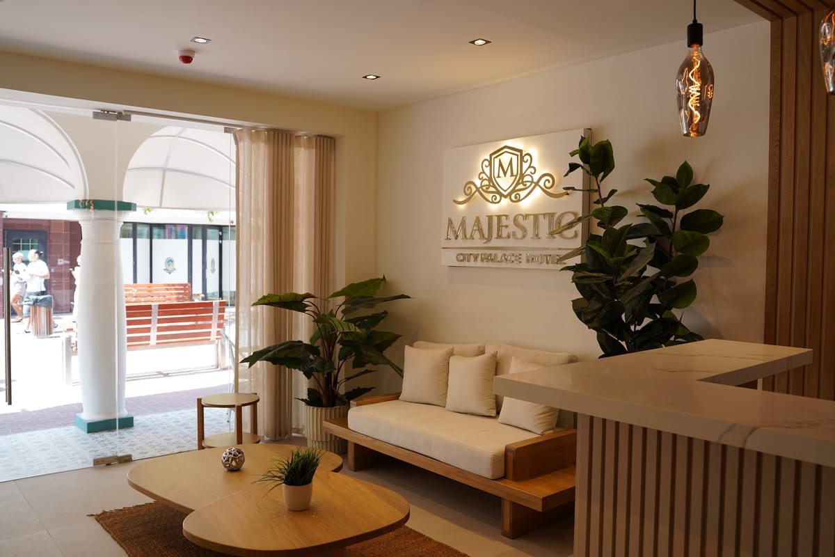 The hotel lobby: a low linen sofa, round oak tables and the lit crest above the reception desk