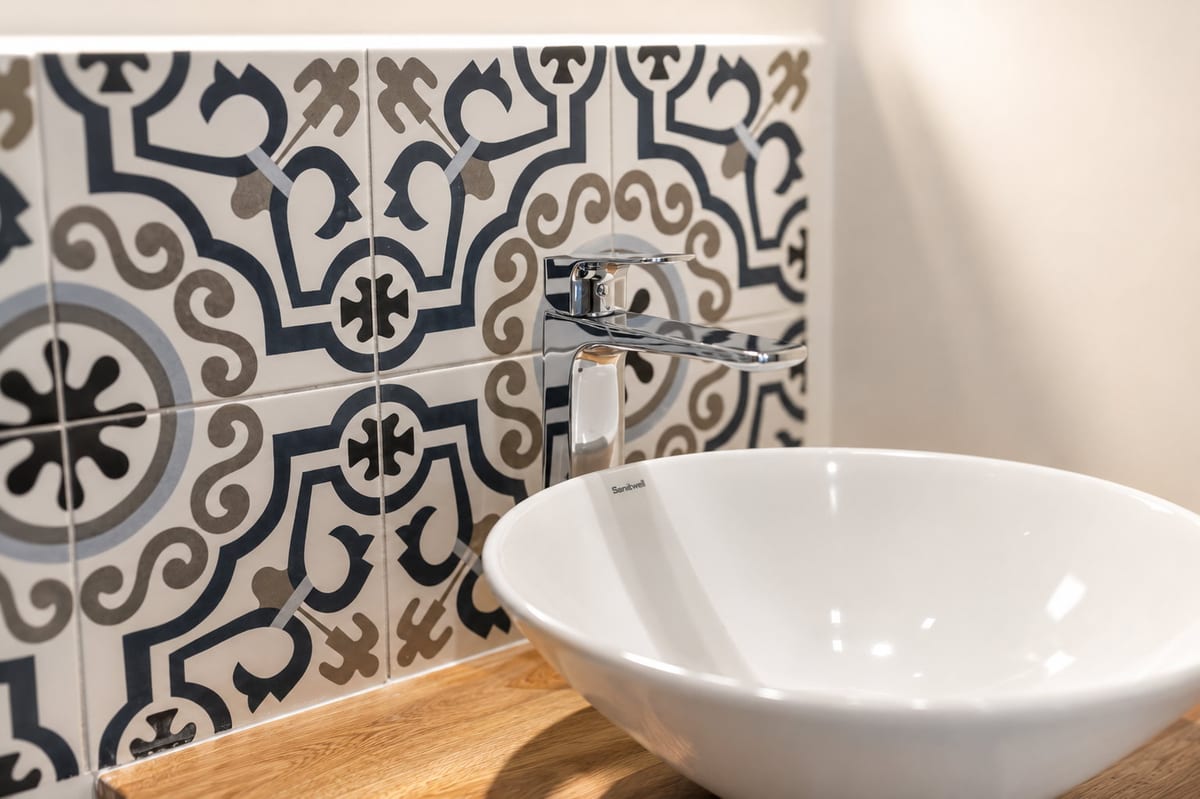 Close up of the majolica splashback behind a loft basin, cobalt, sand and black pattern on a cream ground, with a chrome mixer tap and a white vessel bowl