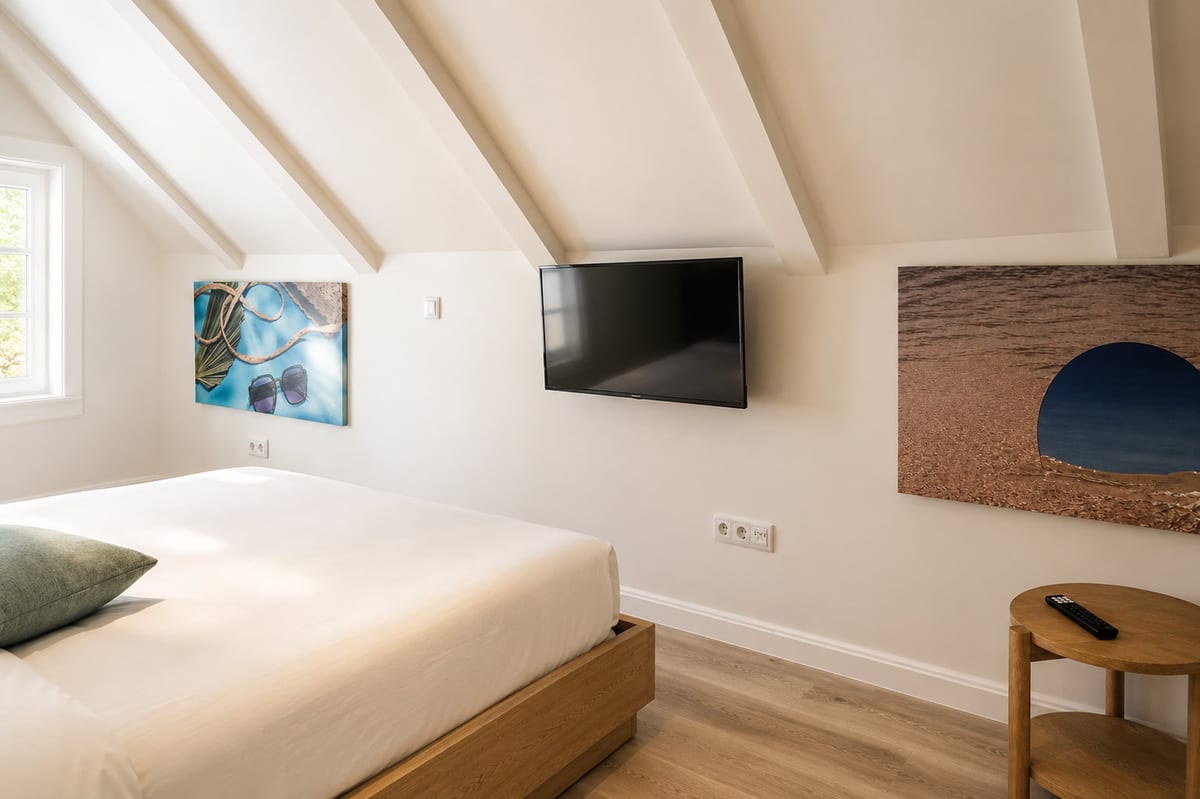The white painted roof beams of the loft over the bed, with two canvases, the television and a round oak side table