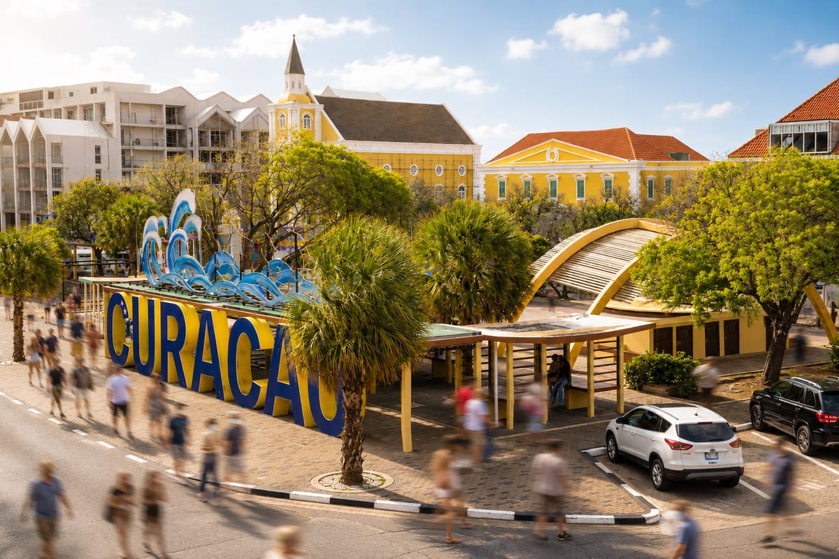 The blue and yellow Curaçao letters on the Punda waterfront with the yellow colonial buildings of Wilhelminaplein behind them and people walking past