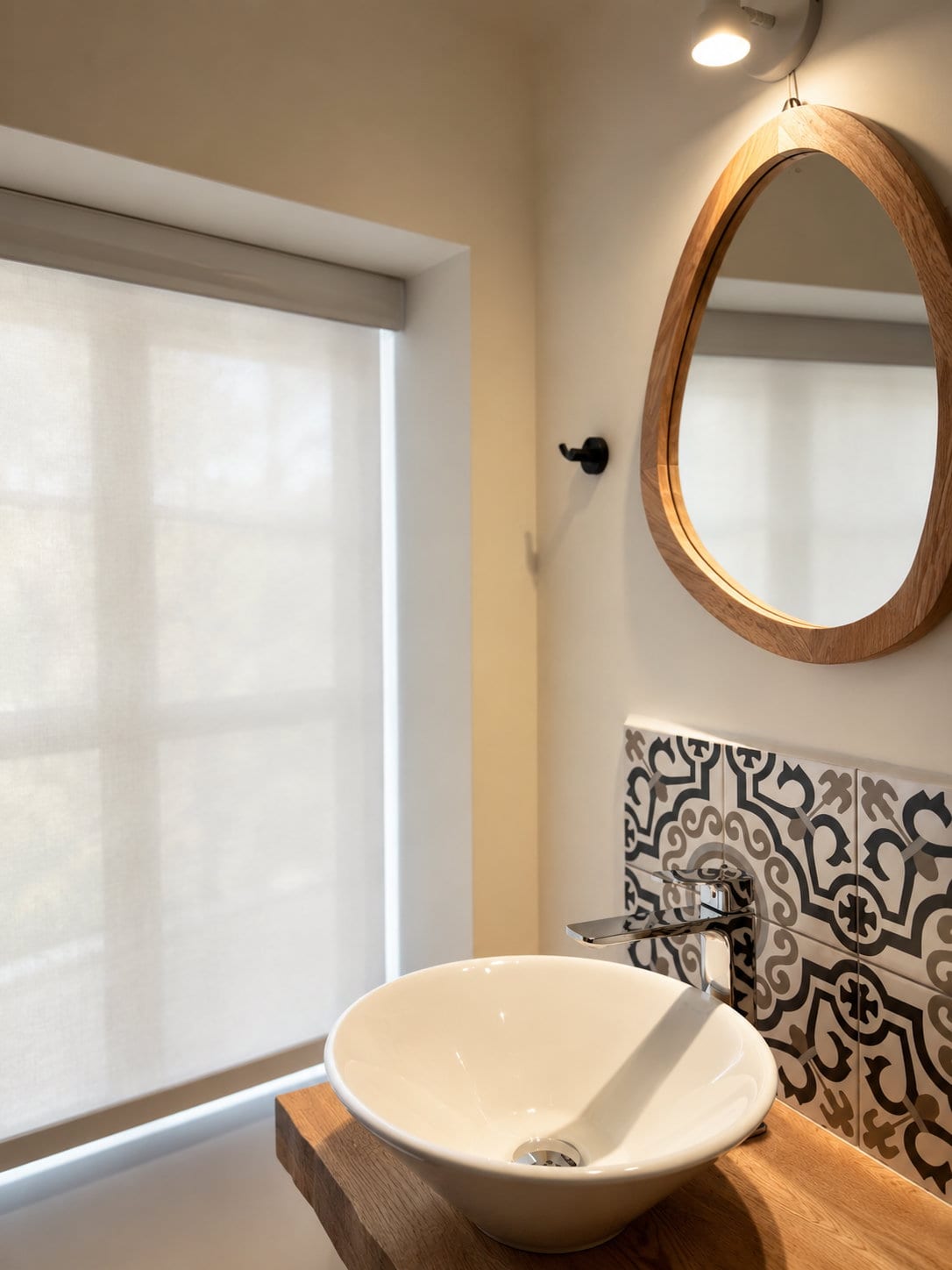 A white vessel basin on an oak shelf against majolica tile, an arched mirror above and a window of soft light beside it